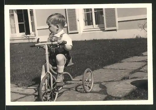Fotografie niedlicher Knabe in Lederhose fährt Dreirad