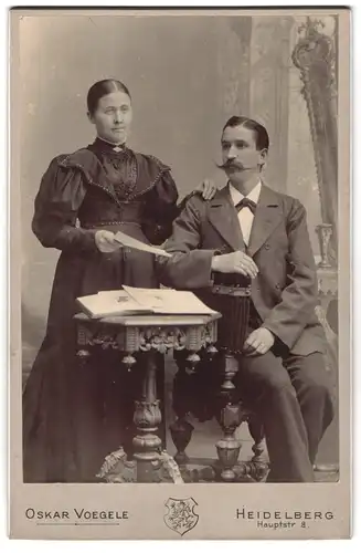 Fotografie Oskar Voegele, Heidelberg, Hauptstr. 8, Mann und Frau in festlicher Kleidung neben aufgeschlagenem Buch