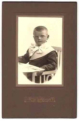Fotografie J. Röttig, Georgswalde i / B., Portrait hübsch gekleideter Junge mit Buch am Tisch sitzend