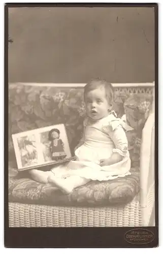 Fotografie Atelier Oberpollinger, München, Portrait niedliches Kleinkind im hübschen Kleid mit Bilderbuch und Puppe