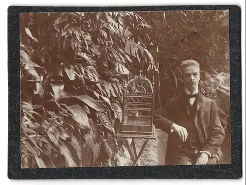 Fotografie unbekannter Fotograf und Ort, junger Mann im Garten mit Vogelkäfig