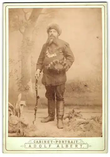 Fotografie Adolf Albert, Bodenbach, Portrait Tscheche in böhmischer Tracht mit Pfeife und Stock vor einer Studiokulisse