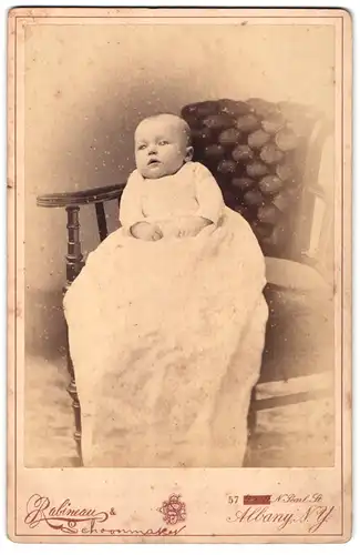 Fotografie Rabineau, Albany, N. Y., 9 & 11, N. Pearl St., Portrait niedliches Baby im weissen Kleid auf Stuhl sitzend