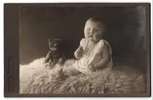 Fotografie Zinserling, Duderstadt, niedliches kleines Baby auf Lammfell mit Teddybär
