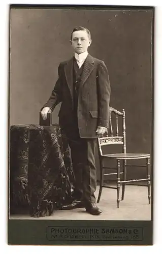 Fotografie Samson & Co., Magdeburg, Breiteweg 168, Portrait junger Mann im Anzug mit Buch an Tisch gelehnt