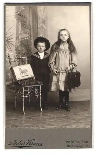 Fotografie Atelier Kranz, Worms a. Rh., Nord-Anlage 17 I., Portrait hübsch gekleidetes Mädchen und Brüderchen mit Ranzen