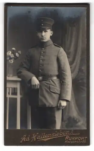 Fotografie Ad. Hallensleben, Ruhrort, Kaiserstr. 10, Portrait junger Soldat in Feldgrau Uniform mit Schirmmütze