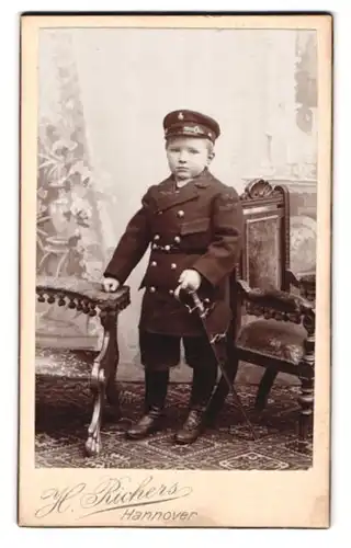 Fotografie H. Richers, Hannover, Cellerstr. 146, Portrait kleiner Junge in Uniform Mantel mit Säbel