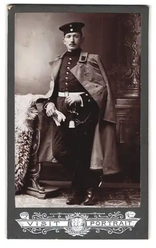 Fotografie unbekannter Fotograf und Ort, Portrait Soldat in Uniform mit Mantel und Krätzchen, Säbel mit Portepee