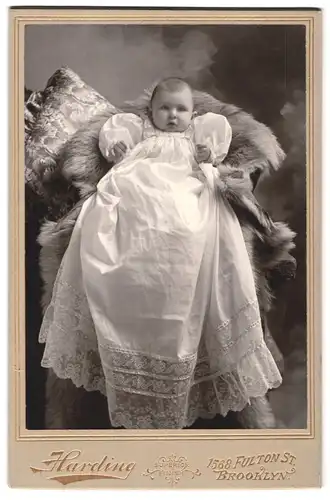 Fotografie Harding, Brooklyn, 1568 Fulton St., Portrait niedliches Baby im weissen Kleid auf Fell sitzend