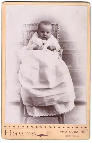 Fotografie Hawes, Anaconda, Portrait niedliches Baby im weissen Kleid im Hochstuhl sitzend