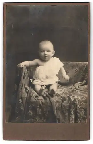 Fotografie unbekannter Fotograf und Ort, Portrait niedliches Kleinkind im weissen Hemd auf Decke sitzend
