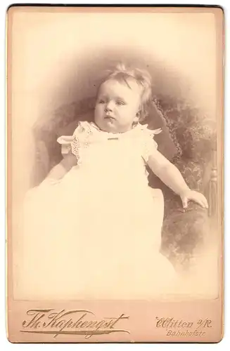 Fotografie Th. Kaphengst, Witten a. R., Bahnhofstrasse, Portrait niedliches Kleinkind im weissen Kleid auf Sessel sitzend