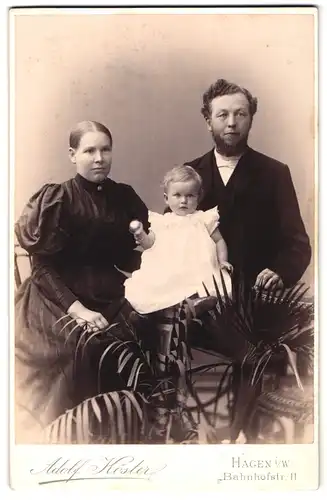 Fotografie Adolf Köster, Hagen i / W., Bahnhofstrasse 11, Portrait bürgerliches Paar und kleine Tochter mit Rassel