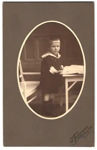 Fotografie A. Fuhrmann, Harburg a / E., Maretstrasse 1, Portrait hübsch gekleideter Junge mit Zeitung an Tisch gelehnt
