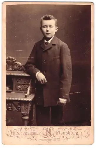 Fotografie H. Kriegsmann, Flensburg, Grosse Strasse 75, Portrait junger Mann im Anzug an Schreibtisch gelehnt
