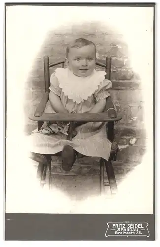 Fotografie Fritz Seidel, Berlin-Spandau, Breitestrasse 35, Portrait niedliches Kleinkind im hübschen Kleid im Hochstuhl