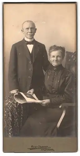 Fotografie Rud. Obest, Salzwedel, Portrait älteres Paar in eleganter Kleidung mit Zeitung am Tisch
