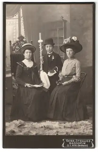 Fotografie Gebr. Strauss, Mannheim, Breitestrasse 6, Portrait Kommunikant mit Kerze und Gebetsbuch zwischen zwei Frauen