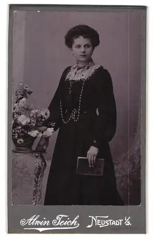 Fotografie Alwin Teich, Neustadt i / S., Portrait bürgerliche Dame mit Blumenkorb an Tisch gelehnt