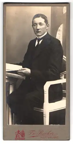 Fotografie Fr. Becker, Höftgrube, Feiner Herr im Anzug mit Scheitelfrisur an einem Tisch sitzend mit Buch in den Händen