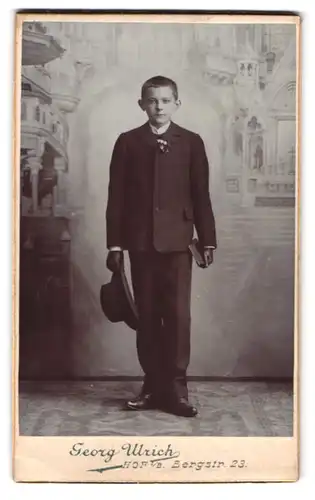 Fotografie Georg Ulrich, Hof i. B., Bergstr. 23, Portrait Junge im Anzug mit Hut und Buch in Studiokulisse