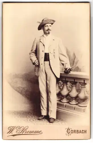 Fotografie W. Stremme, Corbach, Portrait Mann im hellen Anzug mit Fernglas und Federhut, Kummerbund