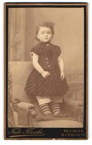 Fotografie Fritz Flaake, Solingen, Portrait niedliches kleines Mädchen im Kleidchen mit gestreiften Söckchen