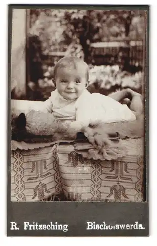 Fotografie R. Fritzsching, Bischofswerda, Portrait süsses Baby im weissen Kleidchen auf Fell liegend