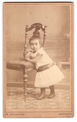 Fotografie Fr. Neumayer, München, Neuhauserstr. 29, Portrait niedliches kleines Mädchen mit Ball am Stuhl stehend