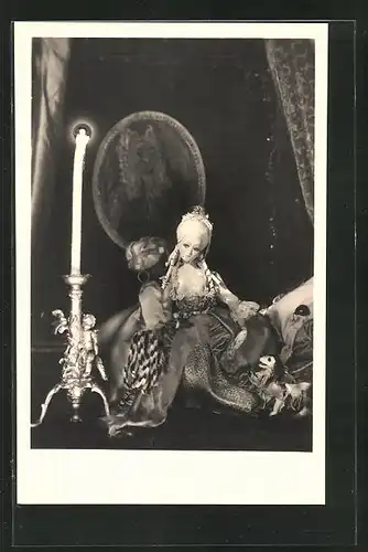 AK hübsche Puppe im barocken Kleid auf einem Puppenbett sitzend