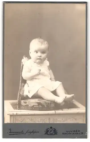 Fotografie P. Jovanovits, Neusatz, Hauptgasse 9, Portrait niedliches Kleinkind im weissen Kleid mit nackigen Füssen