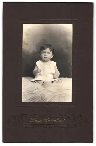 Fotografie unbekannter Fotograf und Ort, Portrait niedliches Kleinkind im weissen Hemd auf Fell sitzend