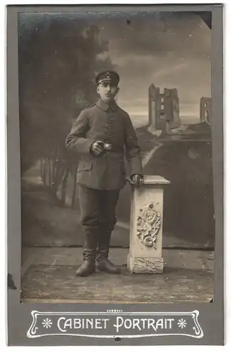 Fotografie unbekannter Fotograf und Ort, Portrait Soldat in Feldgrau Uniform vor einer Studiokulisse