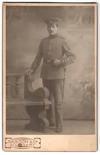 Fotografie Samson & Co., Stuttgart, Königstr. 60, Portrait Soldat in Uniform mit Bajonett vor einer Studiokulisse