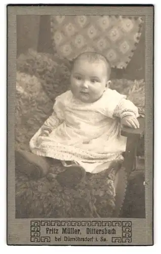 Fotografie Fritz Müller, Dittersbach, Portrait Portrait niedliches Baby im hübschen Kleid auf Fell sitzend