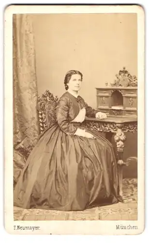Fotografie F. Neumayer, München, Neue Pferdstr. 2, Portrait Frau im seidenen Kleid mit Zöpfen sitzt am Sekretär
