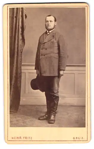 Fotografie Heinr. Fritz, Greiz, Weststr. 6, Portrait korpulenter Mann im Anzug mit Lederstiefel und Zylinder, Vollbart