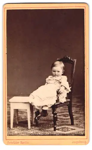 Fotografie Gebr. Martin, Augsburg, Bahnhofstr. 22, Portrait kleines Kind im Rüschenkleid sitzt auf einem Stuhl