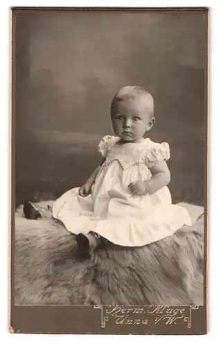 Fotografie Hermann Kluge, Unna i / W., Schäferstrasse 14, Portrait kleines Mädchen im weissen Kleid auf Fell sitzend