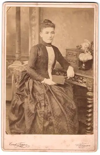 Fotografie Ernst Tepper, Rixdorf, Bergstr. 123, Portrait junge Frau im weiten Kleid mit Hochsteckfrisur am Sekretär