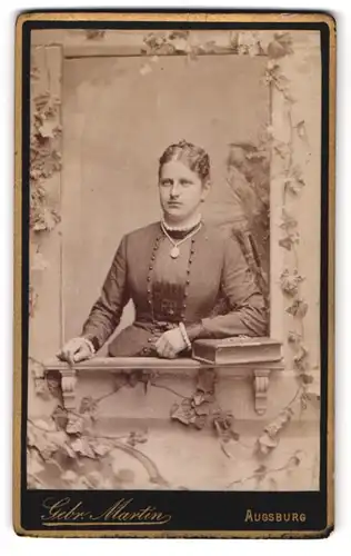 Fotografie Gebr. Martin, Augsburg, Bahnhofstr., Portrait Frau im schicken Kleid mit Kette schaut aus einem Fenster