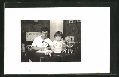 Foto-AK Kinderpaar mit Bilderbuch und Puppen am Tisch sitzend