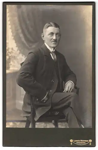 Fotografie Ludwig Mertens, Rendsburg, Portrait stattlicher Herr im Anzug auf Stuhl sitzend