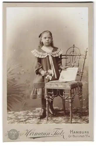 Fotografie Hermann Tietz, Hamburg, Gr. Burstah 12-14, Portrait hübsches Mädchen mit Buch am Stuhl stehend