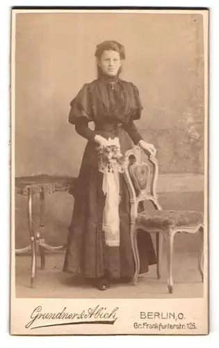 Fotografie Grundner & Abich, Berlin-O, Gr. Frankfruterstrasse 126, Portrait bürgerliche Dame mit Blumen an Stuhl gelehnt