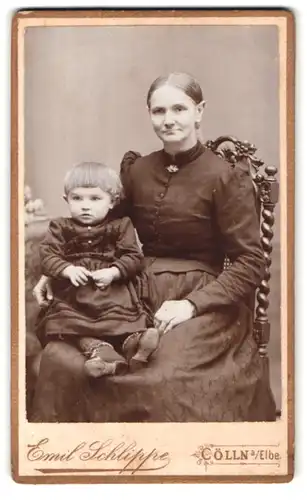 Fotografie Emil Schlippe, Cölln a / Elbe, Dame in Kleid posiert mit Kind mit Topfschnitt auf dem Schoss