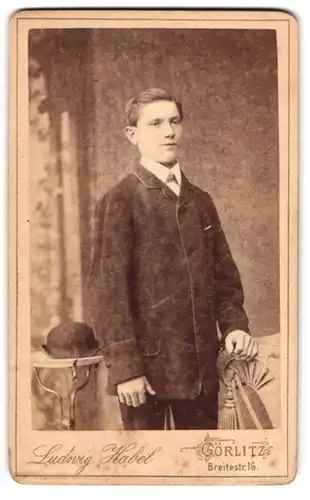 Fotografie Ludwig Habel, Görlitz, Breitestr. 16, Junger Mann mit dicker Jacke steht neben Tisch mit Melone