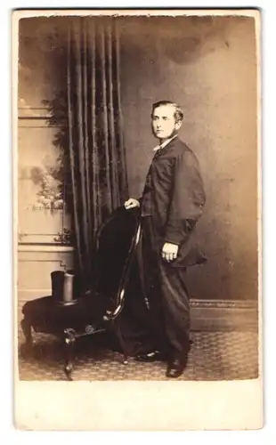 Fotografie Stuart Brothers, Knightsbridge, 47 Bromton Road, Portrait junger Mann im Anzug mit Zylinder auf dem Seesel