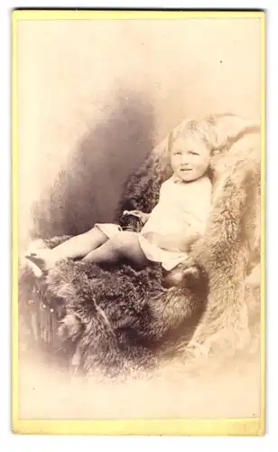 Fotografie E. Shayler, Redcar, 10 Bath St., Portrait kleines Mädchen im weissen Hemd auf Fell sitzend